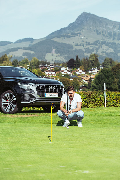 Mann in weißem Polo auf einem Golfplatz vor einem schwarzen Audi