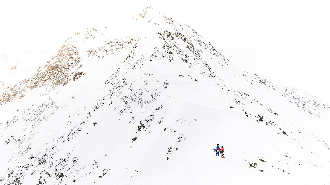 Zwei Snowboarder stehen am Fuße eines schneebedeckten Berges