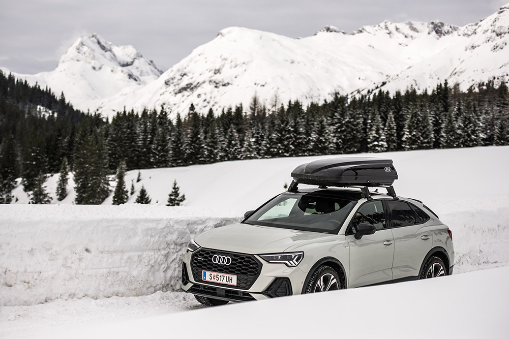 Weißer Audi Q3 mit Dachträger fährt durch eine Schneelandschaft